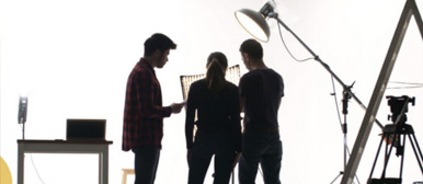 Drei Personen stecken die Köpfe zusammen in einem Filmstudio.