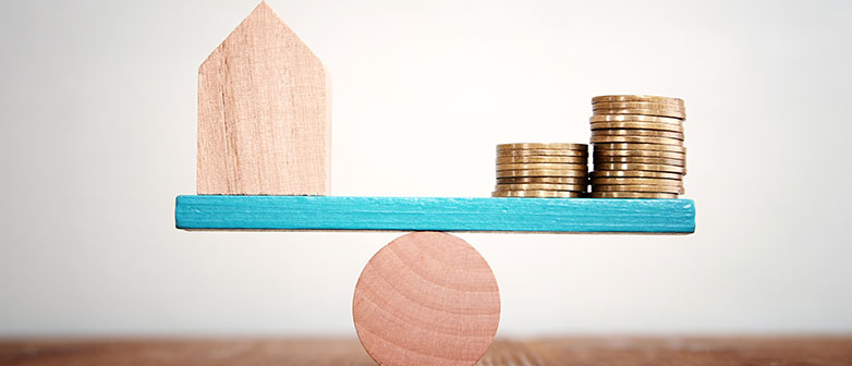 Waage mit Tiny House und Geldmünzen