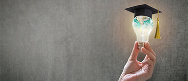 Hand, die eine Glühbirne mit Akademikerhut hält