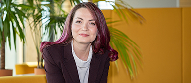 Porträt von Aygul Zagidullina. Sie lächelt freundlich in die Kamera. Aygul hat mittellanges, violett gefärbtes Haar und trägt eine weisse Bluse und einen schwarzen Blazer.