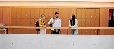 Drei Studierende lehnen an Geländer und sprechen miteinander