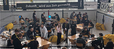 Menschen stehen um grosse Tische in einem offenen Raum