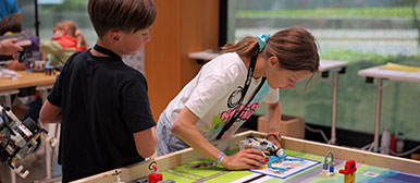 Ein Mädchen und ein Junge stehen an einem Arbeitstisch mit einem Roboter