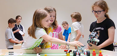 Drei Mädchen stehen an einem Tisch mit einem Roboter drauf