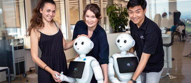 Drei Studierende interagieren mit den beiden Pepper-Roboter. 