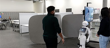 Zwei Studierende schauen auf den Roboter Pepper