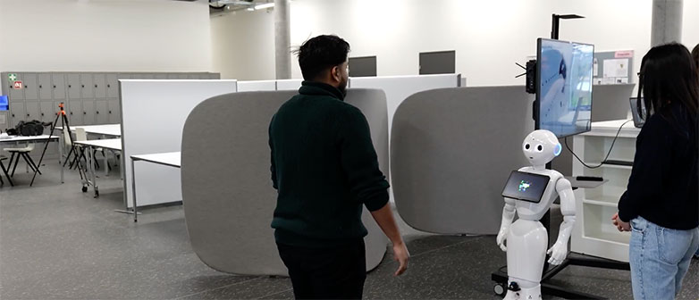Zwei Studierende schauen auf den Roboter Pepper