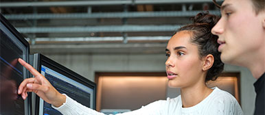 Eine Frau erklärt einem Mann etwas und zeigt dabei auf einen Bildschirm.