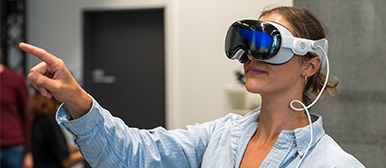 Junge Frau hat VR-Brille an und zeigt mit ihrem Finger nach vorne