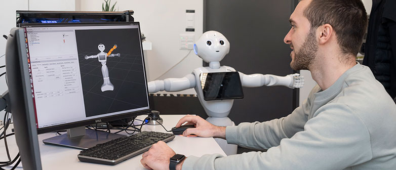 Student vor Laptop mit Roboter nebendran