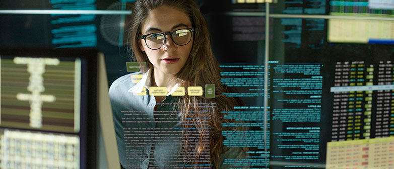 Eine Frau die vor mehreren Bildschirmen am programmieren ist