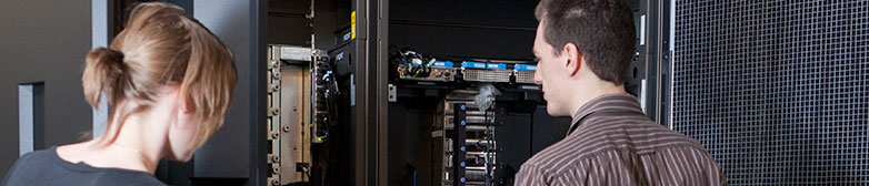 Eine Studentin und ein Student stehe vor dem Mainframe im Enterprise Lab.