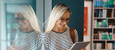 Eine junge blonde Frau blickt lachend auf ihr Tablet