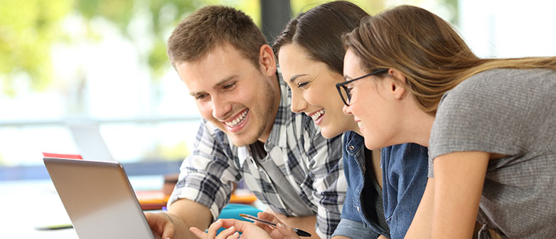 Drei Studierende schauen auf ein Notebook