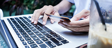 Zwei Hände auf einer Tastatur, eine hält eine EC Karte, die andere tippt