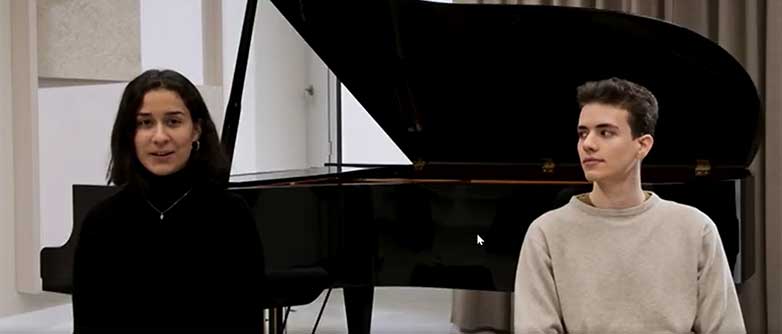 Bild von zwei Studierenden vor einem Klavier. 