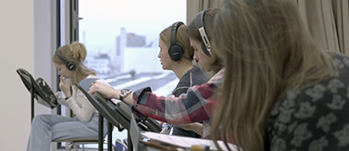 Studierende sitzen in einem Raum und tragen Kopfhörer