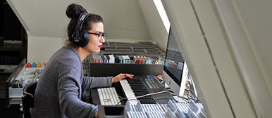 Eine junge Frau sitzt in der Musikbibliothek beim Graben vor einem Computer.