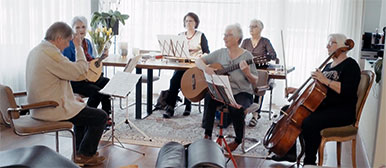 Eine Gruppe Seniorinnen sitzen in einem Wohnzimmer und machen gemeinsam Volksmusik.