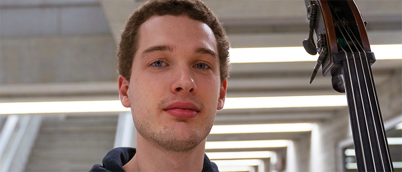 Aliaksei Chvarkou steht im Gebäude des Departements Musik und hält neben sich einen Kontrabass