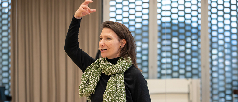 Sarah Keusch steht in einem Ensembleraum und zeigt eine Übung vor