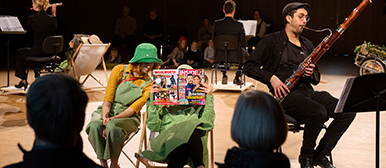 Studierende sitzen auf der Bühne, zwei Studierende tragen grüne Kleider une eine liest ein Heft mit bunten Bildern und dem Titel «Inside»