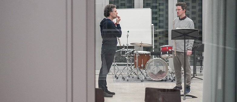 Durch ein Fenster sind zwei Musiker in einem Überaum sichtbar im Gespräch