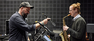 Dominik Burkhalter stellt ein Mikrofon ein, ein Student spielt gegenüber von ihm Saxofon