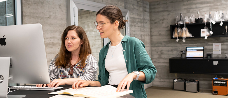 Studierende und Dozent im Hub, vor Bildschirmen und Ausrüstung