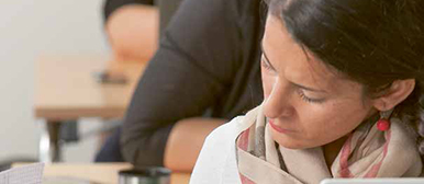 Eine Frau sitzt im Klassenzimmer und schaut in einen Block