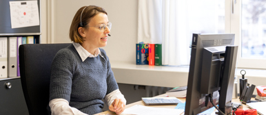 Eine Frau sitzt vor einem Bildschirm und telefoniert mit Headset