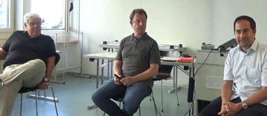 Drei Männer auf Stühlen, die aufmerksam jemandem zuhören