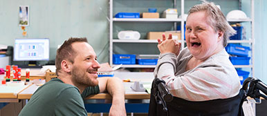 Ein Mann der eine Frau mit Beeinträchtigung anlächelt und sie strahlt ebenfalls  