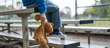 Symbolbild eines Kindes, das mit einem Teddybären auf einer Bank sitzt