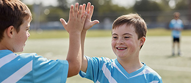 Zwei-Jungs-am-Fussball-spielen-klatschen-ab-behinderung 386x168