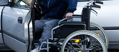 Mann steigt selbständig von seinem Rollstul um in ein Auto