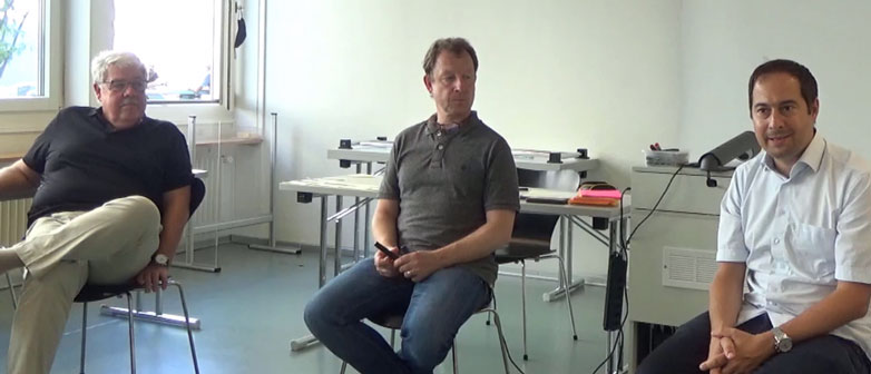 Drei Männer auf Stühlen, die aufmerksam jemandem zuhören