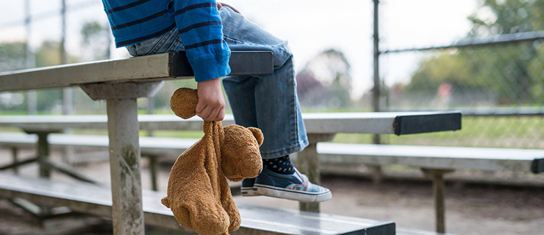 Kind sitzt auf einer Bank mit einem Teddybären in der Hand