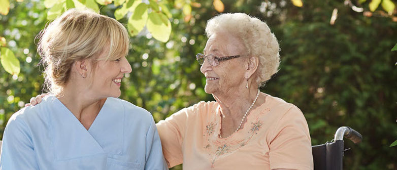 Pflegerin und ältere Frau schauen sich lächelnd an