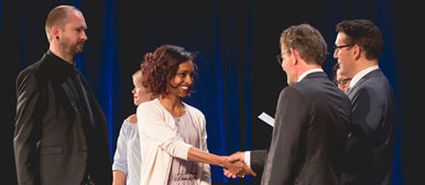 Einer lachenden Studierenden wird ein Diplompreis übergeben 