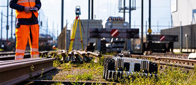 Autonome Systeme und Robotik: Mann in Arbeitskleidung steht auf Bahngleis mit dem Controller für den mobilen Roboter nebendran in der Hand