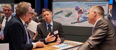 Drei Männer stehen um einen Tisch an einer Messe und diskutieren über Mechanische Systeme.