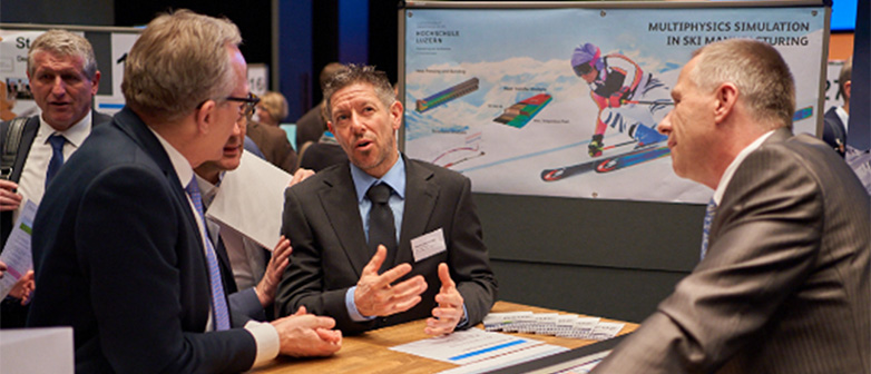 Drei Männer stehen um einen Tisch an einer Messe und diskutieren über Mechanische Systeme.