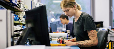 Young female researcher with tattoos testing electrical engineering equipment