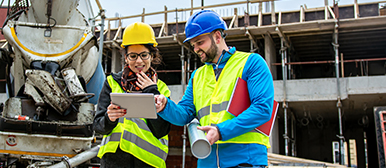 Eine Frau und ein Mann in neongrüner Veste auf einer Baustelle, die sich zusammen einen Plan betrachten 