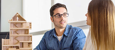 Ein Mann und eine Frau diskutieren neben einem Holzmodell eines Hauses