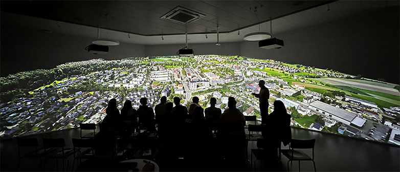 Eine Gruppe Menschen steht in einem dunklen Raum vor einer Projektion