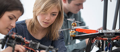 Zwei Studentinnen und ein Student im verschwommenen Hintergrund arbeiten konzentriert an einem technischen Projekt