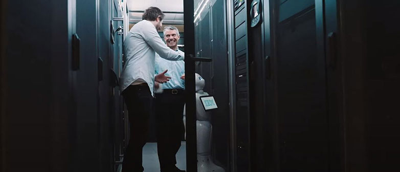 Zwei Männer und ein Roboter vor einem Computerschrank