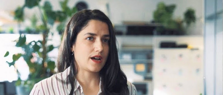 Woman speaking in a bright office with plants in the background.